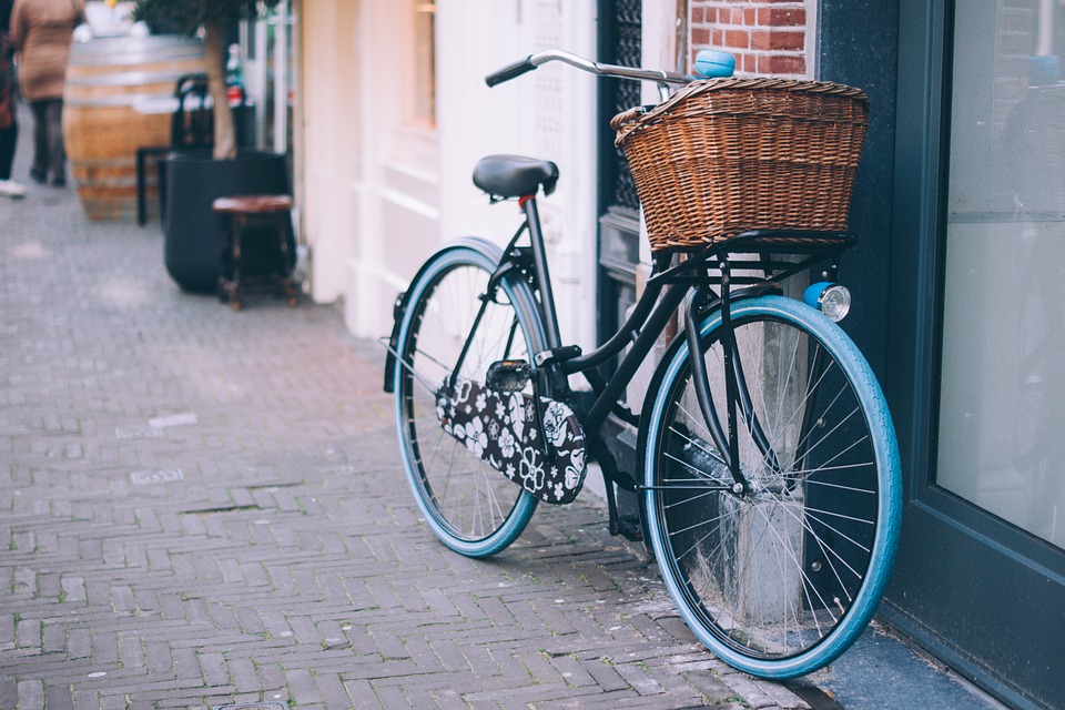 A black and blue bike with a basket is propped up against a wall outside